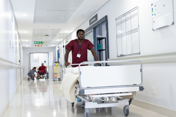 African american male medical worker pushing empty bed in hospital corridor