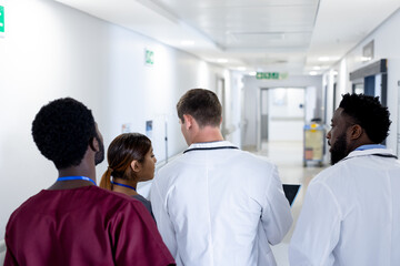 Rear view of diverse group of doctors in discussion, walking in hospital corridor