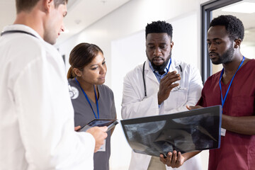 Unaltered portrait of four serious diverse doctors with tablet and x ray talking in hospital