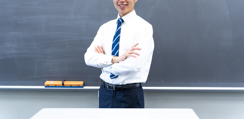 黒板の前で腕組をする男性の先生