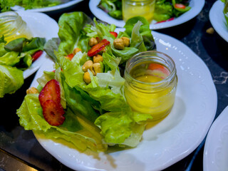 Salad of different types of lettuce, chopped strawberries, hazelnuts and salad dressing in a glass jar on a white plate. catering event on some festive event, party or wedding, in a restaurant. Buffet