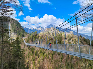 Fototapeta na wymiar Pedestrian Swinging Bridge in Austria, with Historic Castle and Alps in Background