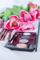 Obraz na płótnie Canvas Pink tulips, eye shadow palette with mirror, brushes on white background, women makeup cosmetics set