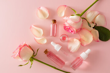 Several different glass cosmetic bottles with serum with rose petal extract and rose water for facial skin care. The top view is flat styling.