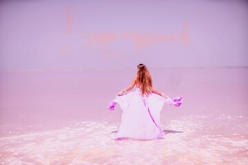 Woman pink salt lake. Against the backdrop of a pink salt lake, a woman in a long pink dress takes a leisurely stroll along the white, salty shore, capturing a wanderlust moment.