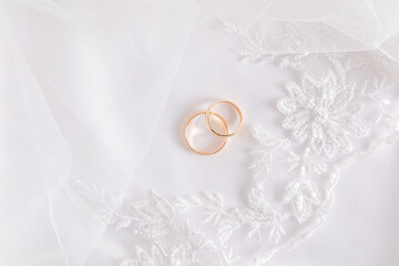 White wedding tulle background with embroidery with two gold wedding rings. Top view. A copy of the space.