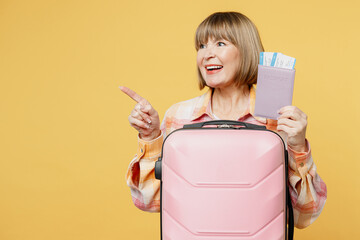 Traveler elderly woman 50 years old wearing casual clothes hold bag passport ticket isolated on plain yellow background. Tourist travel abroad in free spare time rest getaway. Air flight trip concept.