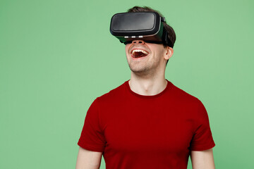 Young surprised caucasian amazed vhappy fun man he wears red t-shirt casual clothes watching in vr headset pc gadget isolated on plain pastel light green background studio portrait. Lifestyle concept. - Powered by Adobe