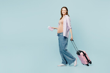 Full body young pregnant mom woman with belly tummy wear casual clothes hold bag passport ticket isolated on plain blue background. Tourist travel abroad in free time rest getaway. Air flight concept.