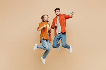 Full body young couple two friend family man woman wear casual clothes together doing selfie shot on mobile cell phone post photo on social network jump high isolated on pastel plain beige background