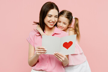 Happy smiling woman wear casual clothes with child kid girl 6-7 years old. Daughter give mother postcard with heart, hug and cuddle isolated on plain pastel pink background. Family parent day concept.