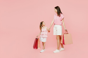 Full body young woman wear casual clothes with child kid girl 6-7 years old hold shopping bag going...