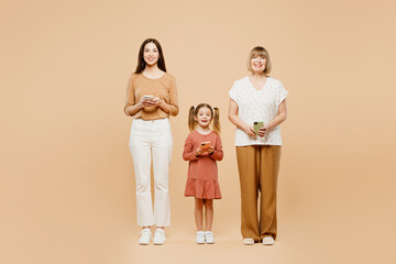 Full body happy women wearing casual clothes with child kid girl 6-7 years old. Granny mother daughter hold in hand use mobile cell phone isolated on plain beige background. Family parent day concept.