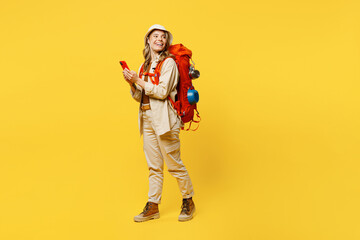 Fototapeta na wymiar Full body sideways young woman carry bag with stuff mat use mobile cell phone isolated on plain yellow background Tourist lead active lifestyle walk on spare time. Hiking trek rest travel trip concept