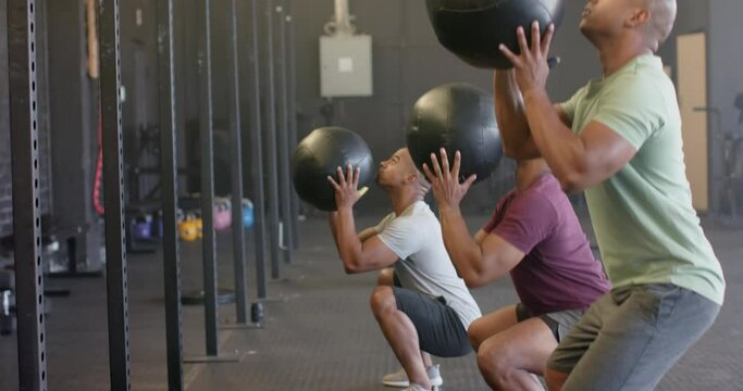 Diverse male group fitness class training at gym lifting and throwing medicine balls, in slow motion