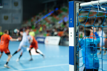 Detail of handball goal post with net and players in the background. - obrazy, fototapety, plakaty