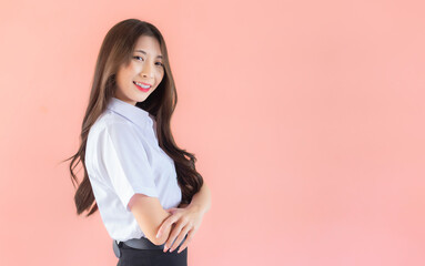 Portrait of young Thai student in university student uniform. Asian cute girl standing with her arms crossed confidently isolated on peach color background.