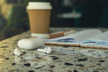 Take away coffee in craft recycling paper cup with paper notebook with wireless headphones. Mockup Coffee break. Audio healing, sound therapy wellness rituals, positive mental health habits listening