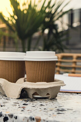 Fototapeta na wymiar Two paper cups with lid for tea to go. Coffee take away on the table. Take-out coffees with brown paper cup holder. Brown safety cardboard collars. Take away box for cups. Cardboard tray