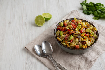 Homemade Grilled Corn Summer Pasta Salad in a Bowl on a white wooden background, low angle view. Copy space.