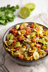Homemade Grilled Corn Summer Pasta Salad in a Bowl on a white wooden background, low angle view. Close-up.
