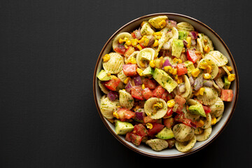 Homemade Grilled Corn Summer Pasta Salad in a Bowl on a black background, top view. Copy space.