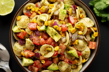 Homemade Grilled Corn Summer Pasta Salad in a Bowl on a black background, top view.
