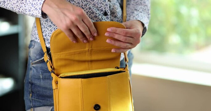 Female employee puts smartphone into mustard color leather handbag ready to go home after work. Woman stands in office near bright window slow motion