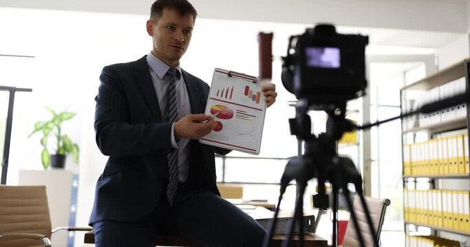 Business coach shows diagram to camera recording video guide in office slow motion. Trainer explains economy principles for university students