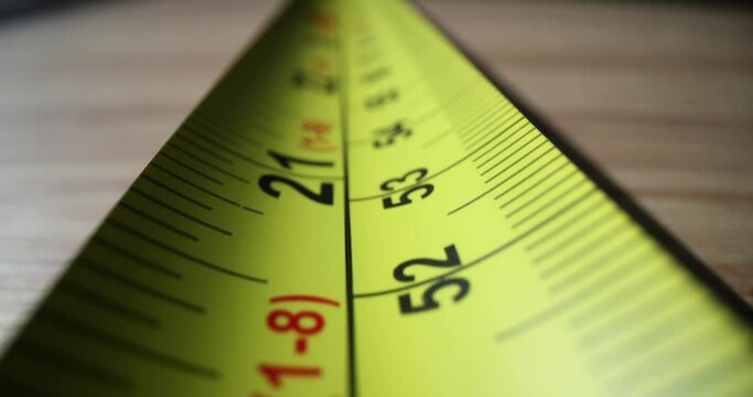 Long yellow centimeter tape-line stretching on wooden table ready for measurement. Ruler with centimeter and inch digits and fractions for measuring length