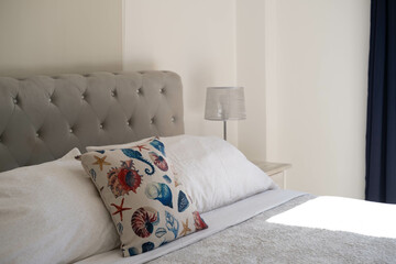 A pillow with a shell print on the bed in the hotel, next to a window with a view of the rainforest, a marine-style interior.