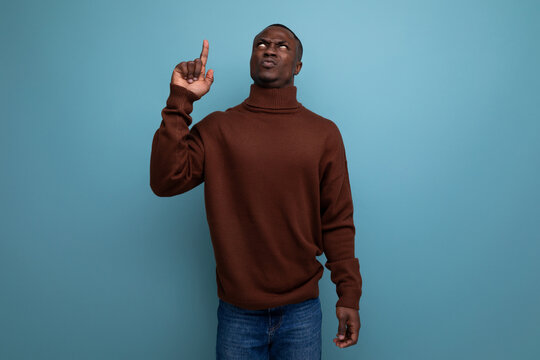 Smart Dark-skinned 25 Year Old American Man With Short Haircut In A Brown Sweater Shows His Hand At An Idea On A Studio Background With Copy Space