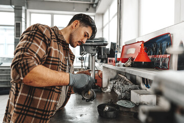 Young man mechanic repairing car parts on worktable in car service shop