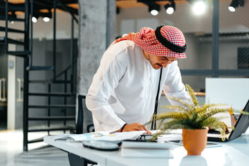 Fototapeta na wymiar Young muslim businessman in traditional outfit working at the table in office