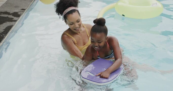 Happy african american mother and daughter playing in swimming pool in garden, slow motion