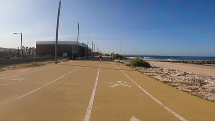 wide and close view of shirtless man energetically runs along the Costa da Caparica beach, with the seawall stretching out beside him - Powered by Adobe