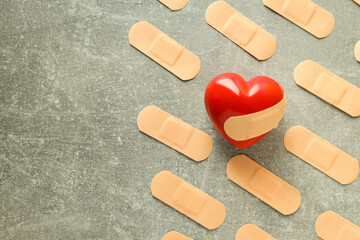 Red heart and adhesive plaster on gray textured background