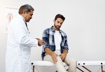 Healthcare, doctor and patient with knee pain in consultation for expert advice, information and discussion. Medicine, health care and Indian man in doctors office consulting medical professional. - obrazy, fototapety, plakaty