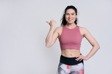 Beautiful female athlete smiling looking at camera, pointing aside at copy space on white background