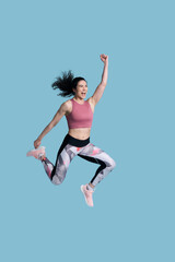 Fototapeta na wymiar Cheerful determined female athlete in sportswear, smiling and jumping high on blue background