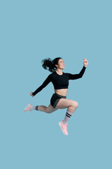 Fototapeta na wymiar Full length side studio portrait of a sportswoman, running fast over blue background. Sport. Fitness