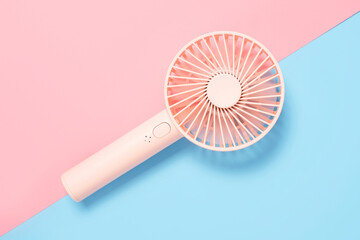 Small portable mini fan on blue and pink background close-up, top view.