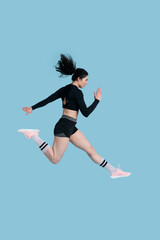 Side portrait athlete woman in black sportswear runs over blue background. People. Sport. Endurance