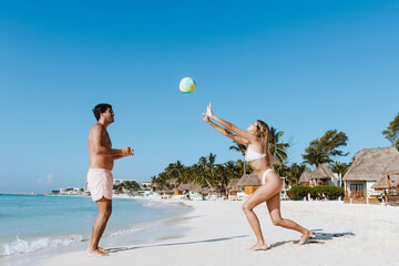 hispanic young couple playing with racket and beach ball together and having fun at caribbean mexican beach in Mexico Latin America