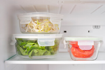 Greens and vegetables in glass containers in the refrigerator, food storage concept.