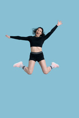 Fototapeta na wymiar Full length portrait smiling sportive athlete woman, jumping high up over blue isolated background