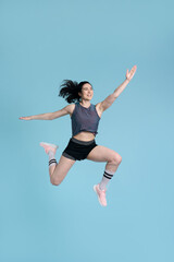 Fototapeta na wymiar Determined, competitive sportswoman, jumping high up, stretching, exercising over blue background