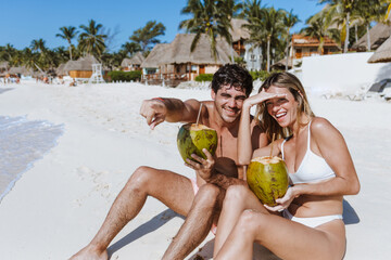 Hispanic young couple holding a coconut and having fun on caribbean beach in holidays or vacations...