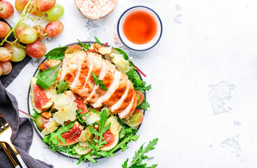 Gourmet salad with fresh figs and grilled chicken fillet, grape, arugula, chard with wine vinegar dressing. White kitchen table background, top view
