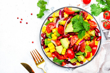 Spicy salad with sweet corn, red beans, avocado, jalapeno, cherry tomatoes, red onion and cilantro. White table background, top view